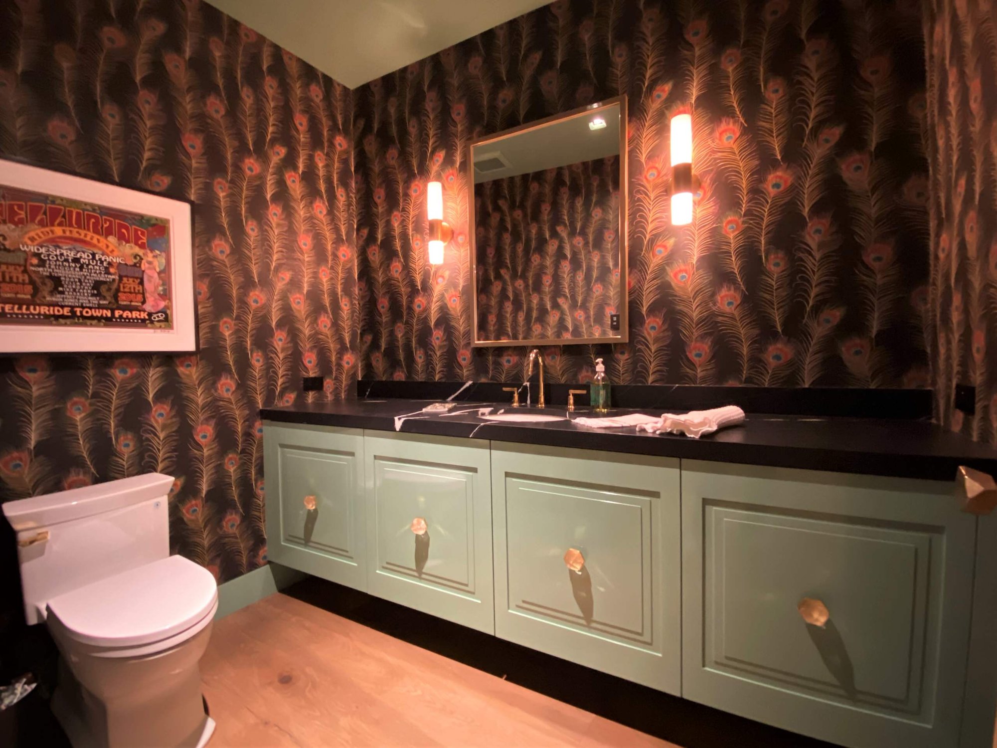 Mid-sized eclectic 3/4 light wood floor, brown floor, single-sink and wallpaper bathroom with raised-panel cabinets, green cabinets, a two-piece toilet, an undermount sink, black countertops and a floating vanity, by Jensen Design in Telluride, CO