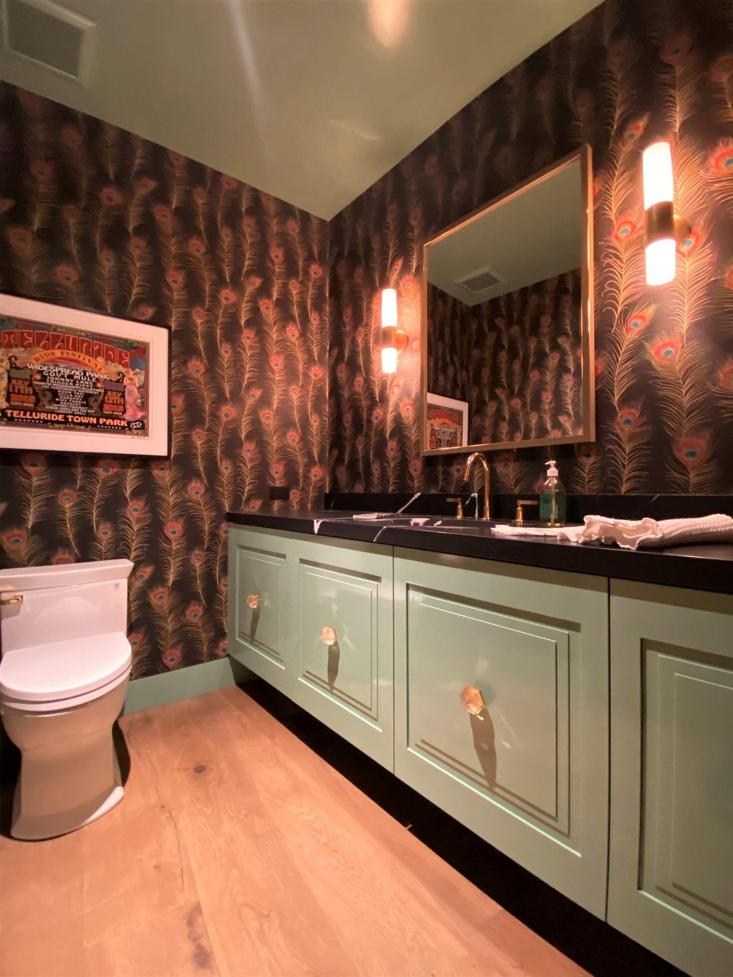Mid-sized eclectic 3/4 light wood floor, brown floor, single-sink and wallpaper bathroom with raised-panel cabinets, green cabinets, a two-piece toilet, an undermount sink, black countertops and a floating vanity, by Jensen Design in Telluride, CO