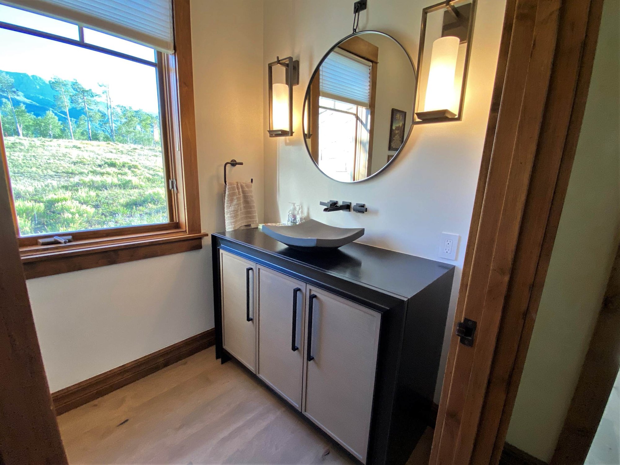 Small transitional 3/4 single-sink bathroom with recessed-panel cabinets, medium tone wood cabinets, white walls, a vessel sink, black countertops and a freestanding vanity, by Jensen Design in Telluride, CO