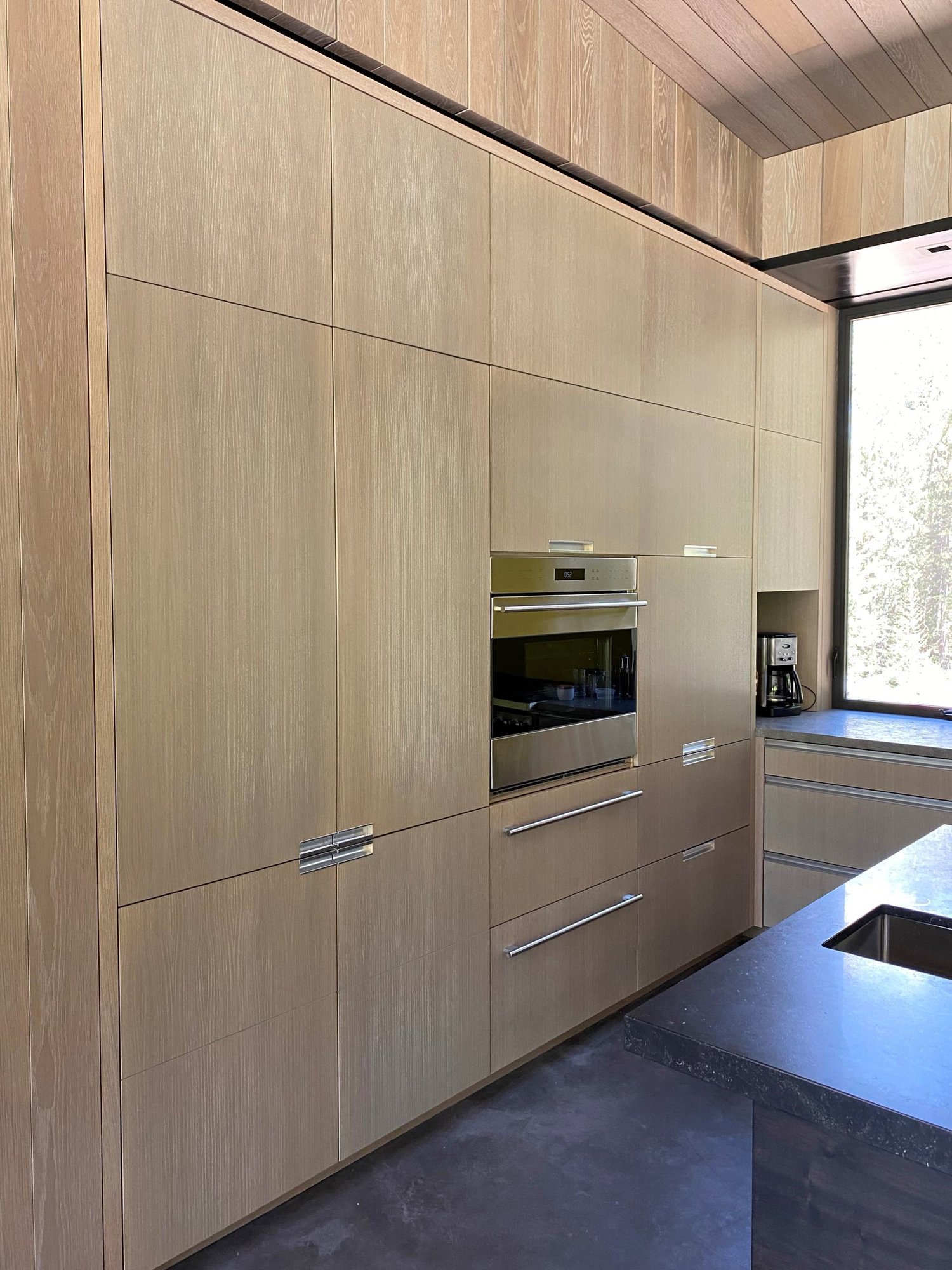 Large trendy u-shaped concrete floor, gray floor and wood ceiling open concept kitchen with an undermount sink, flat-panel cabinets, light wood cabinets, yellow backsplash, glass sheet backsplash, paneled appliances, an island and gray countertops, by Jensen Design in Telluride, CO
