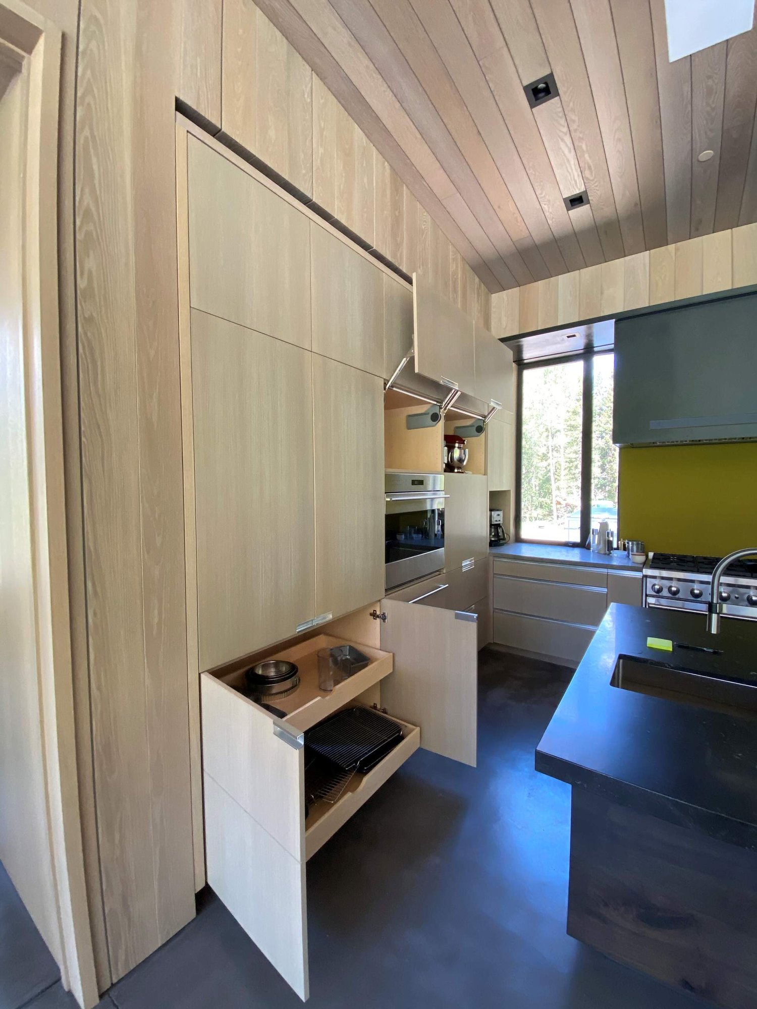 Large contemporary u-shaped concrete floor, gray floor and wood ceiling open concept kitchen with an undermount sink, flat-panel cabinets, light wood cabinets, yellow backsplash, glass sheet backsplash, paneled appliances, an island and gray countertops, by Jensen Design in Telluride, CO