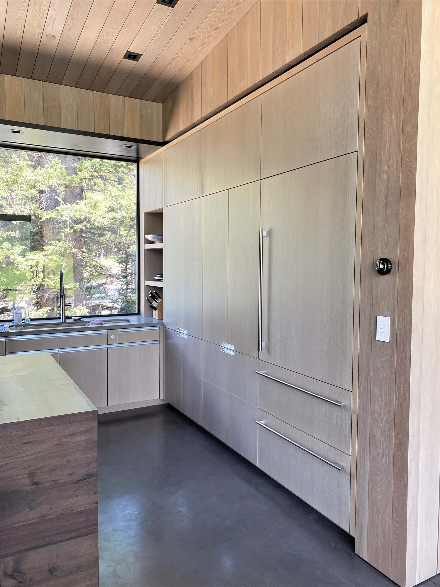 Large contemporary u-shaped concrete floor, gray floor and wood ceiling open concept kitchen with an undermount sink, flat-panel cabinets, light wood cabinets, yellow backsplash, glass sheet backsplash, paneled appliances, an island and gray countertops, by Jensen Design in Telluride, CO