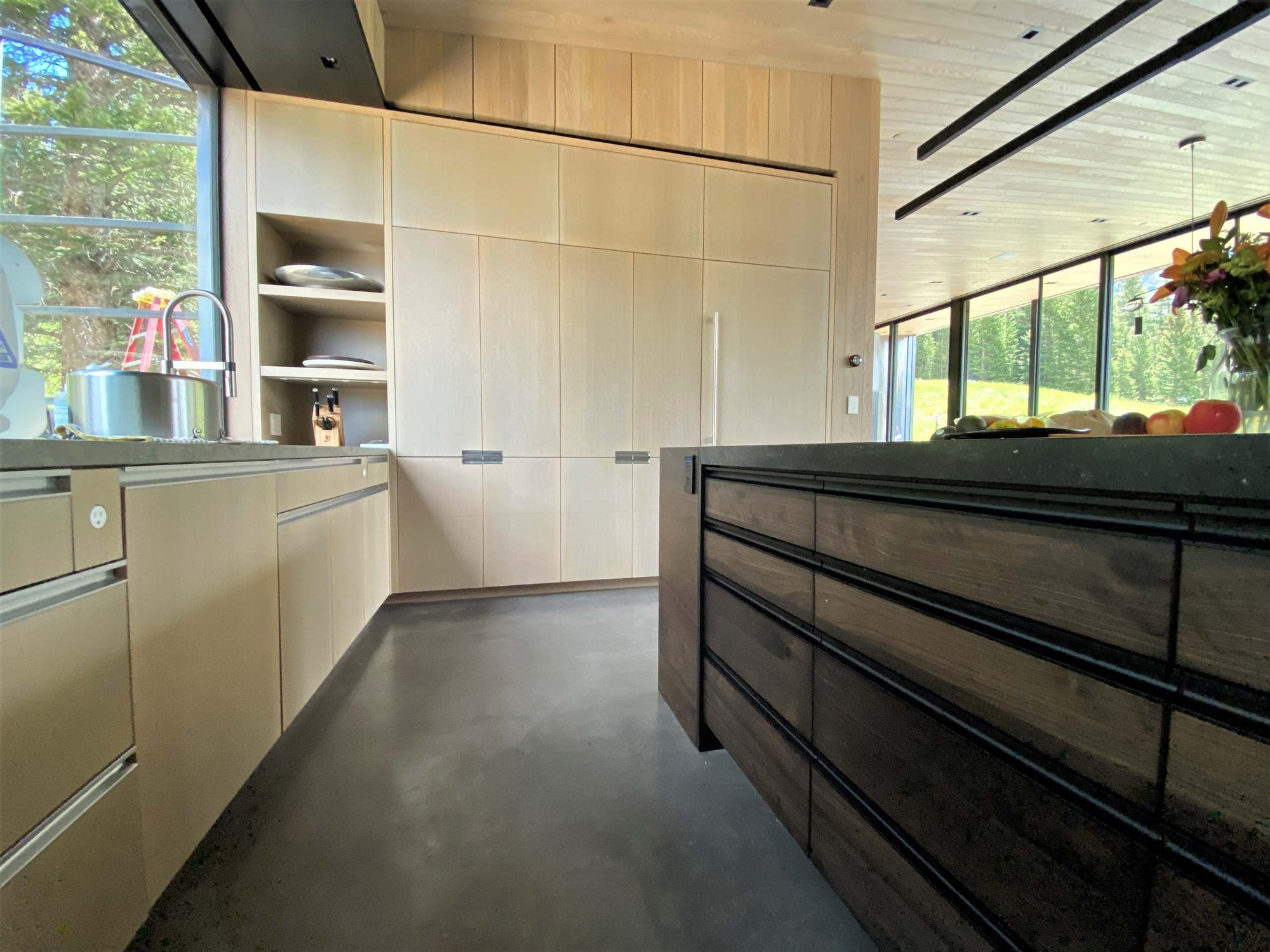 Large trendy u-shaped concrete floor, gray floor and wood ceiling open concept kitchen with an undermount sink, flat-panel cabinets, light wood cabinets, yellow backsplash, glass sheet backsplash, paneled appliances, an island and gray countertops, by Jensen Design in Telluride, CO