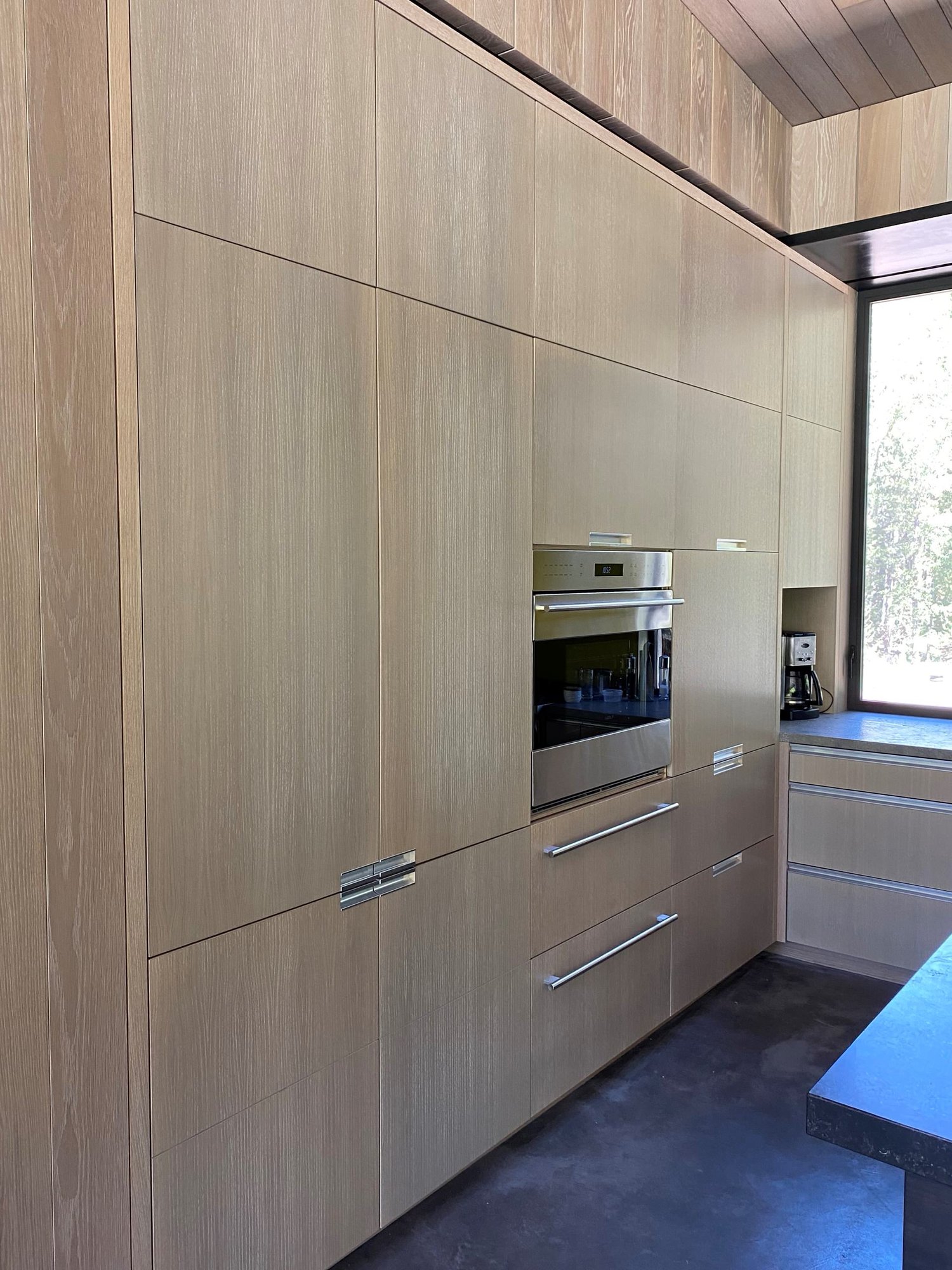 Large trendy u-shaped concrete floor, gray floor and wood ceiling open concept kitchen with an undermount sink, flat-panel cabinets, light wood cabinets, yellow backsplash, glass sheet backsplash, paneled appliances, an island and gray countertops, by Jensen Design in Telluride, CO