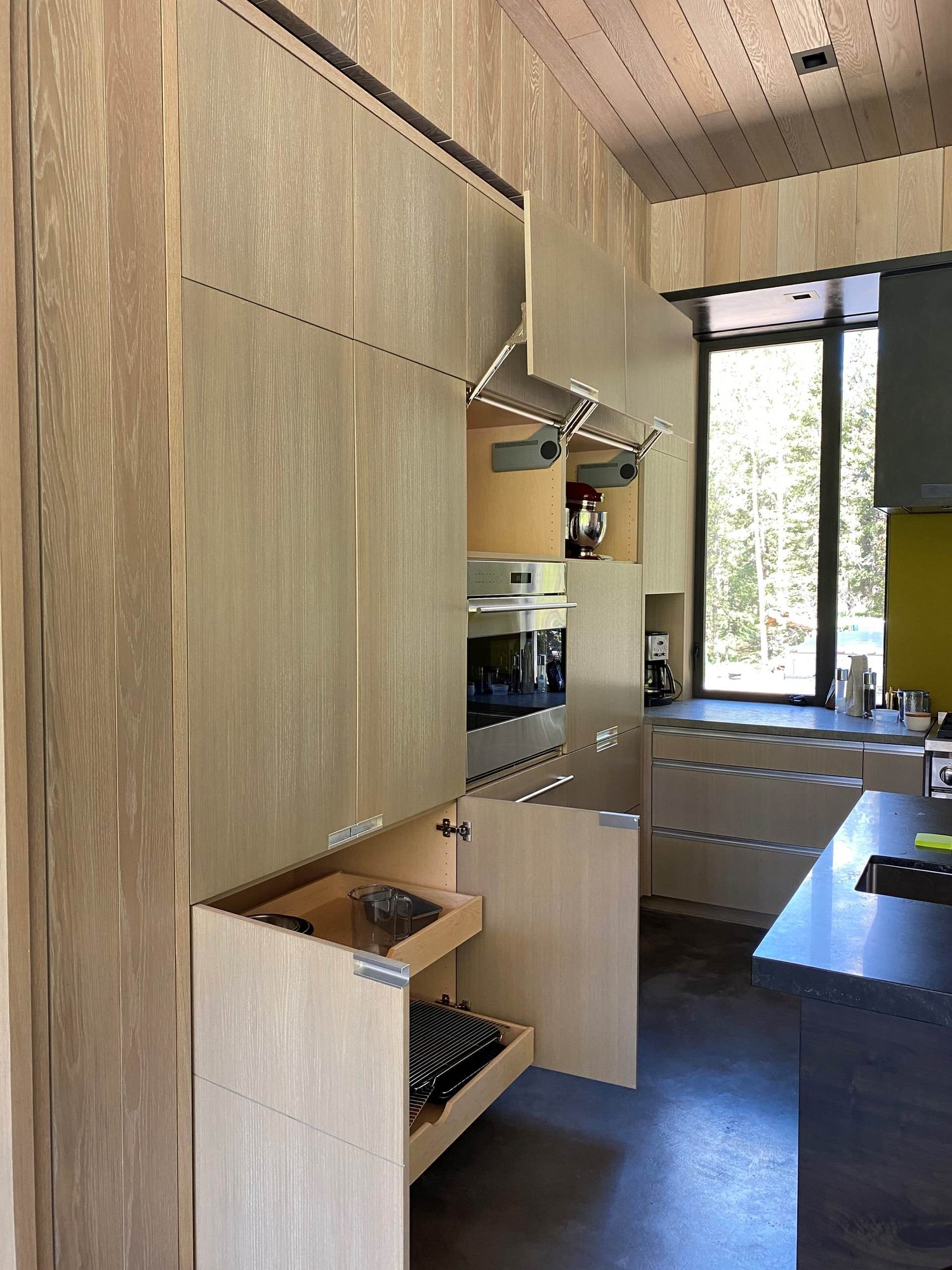 Large contemporary u-shaped concrete floor, gray floor and wood ceiling open concept kitchen with an undermount sink, flat-panel cabinets, light wood cabinets, yellow backsplash, glass sheet backsplash, paneled appliances, an island and gray countertops, by Jensen Design in Telluride, CO