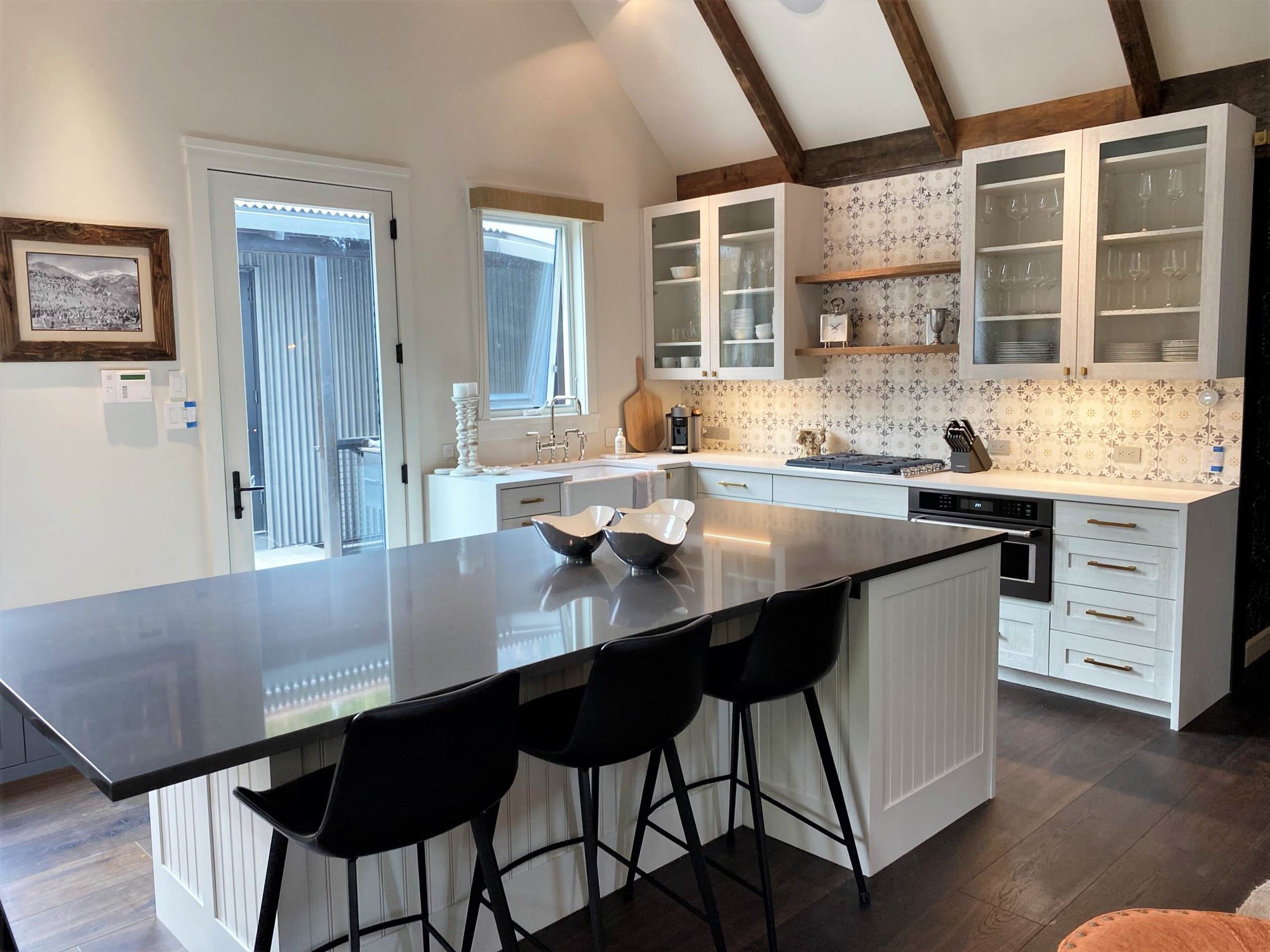 Mid-sized trendy l-shaped dark wood floor, brown floor and vaulted ceiling open concept kitchen with a farmhouse sink, recessed-panel cabinets, white cabinets, white backsplash, paneled appliances and an island, by Jensen Design in Telluride, CO