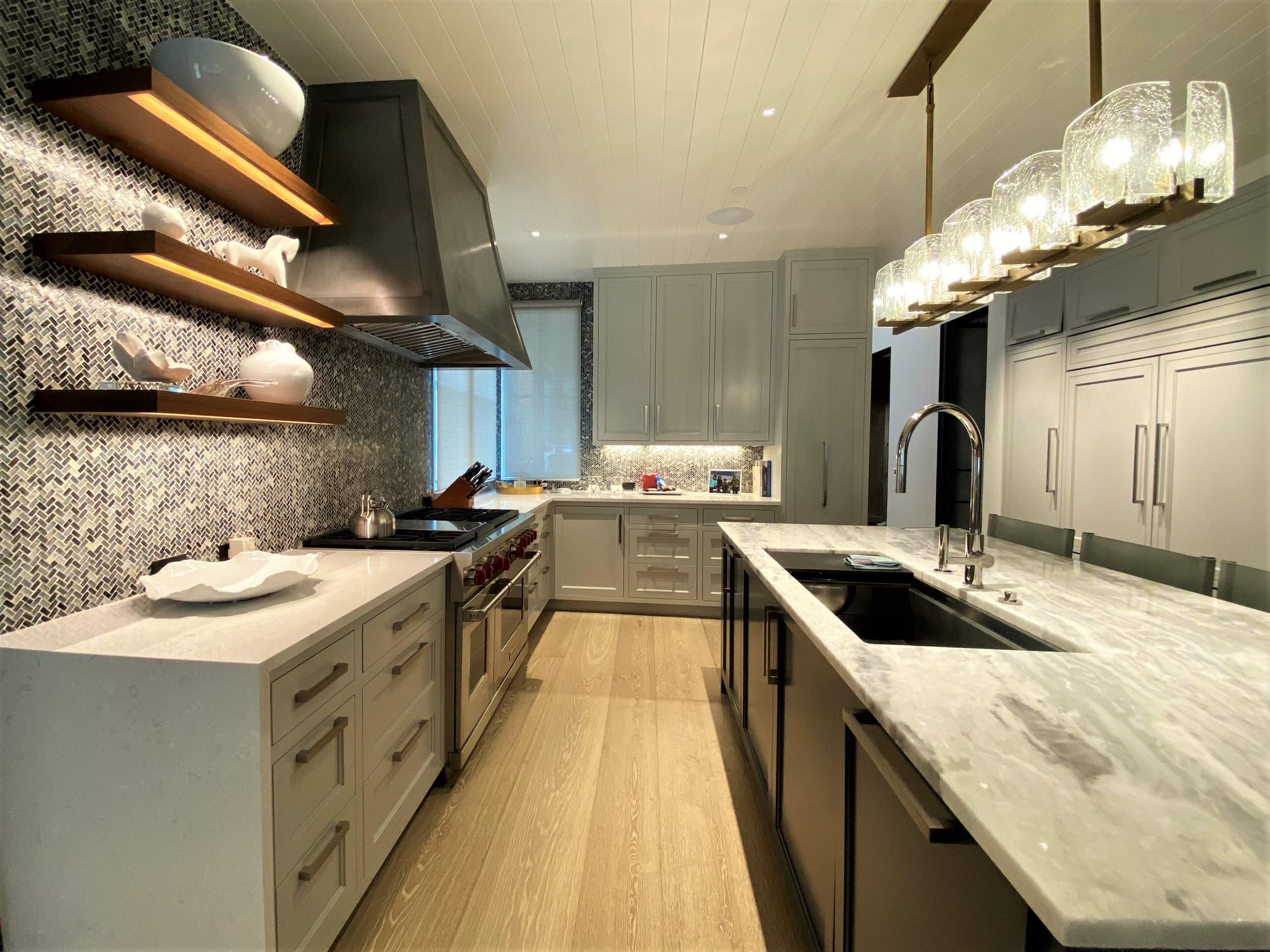 Large trendy u-shaped light wood floor, brown floor and shiplap ceiling open concept kitchen with an undermount sink, recessed-panel cabinets, white cabinets, gray backsplash, paneled appliances, an island and white countertops, by Jensen Design in Telluride, CO