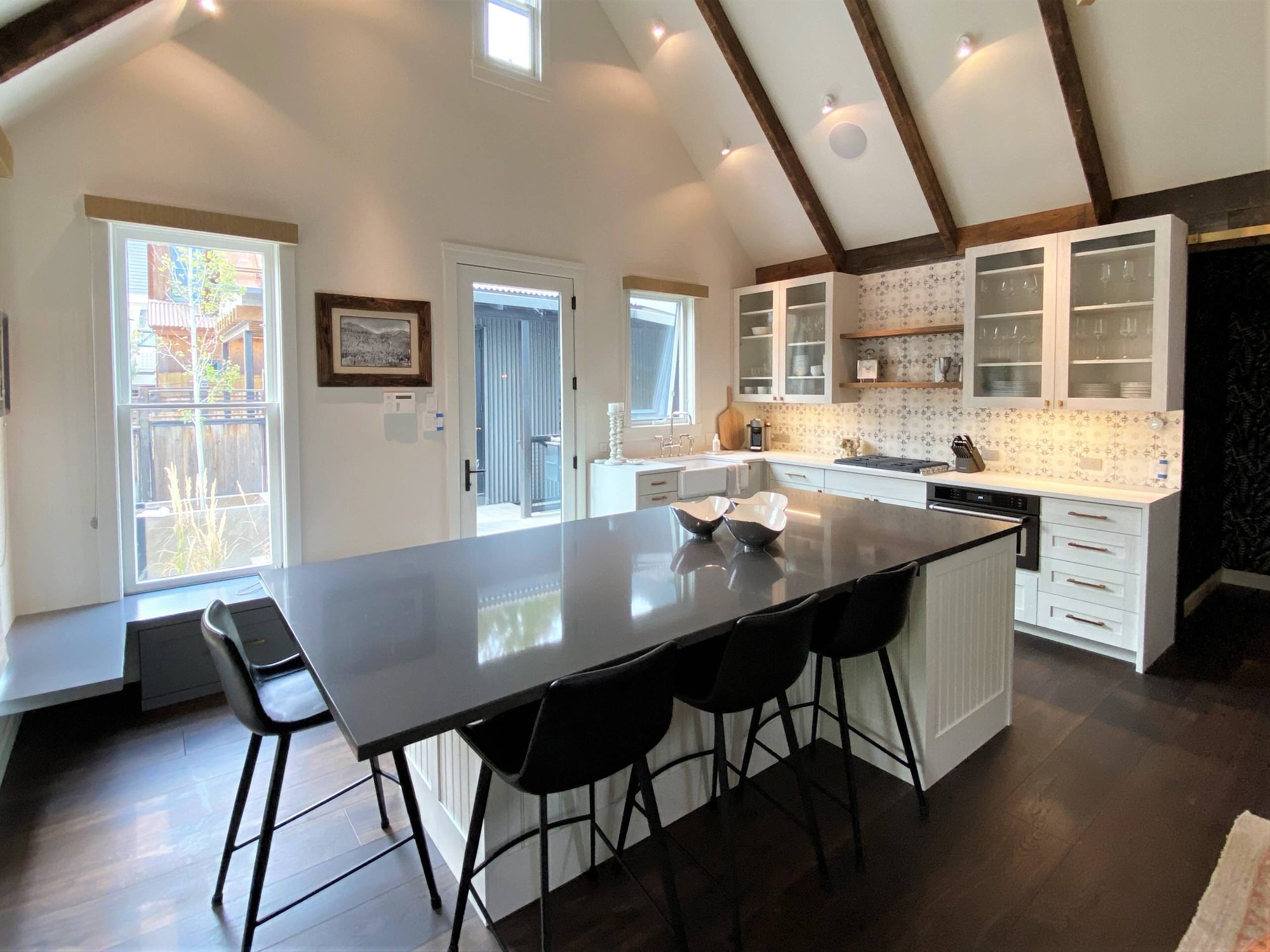 Mid-sized contemporary l-shaped dark wood floor, brown floor and vaulted ceiling open concept kitchen with a farmhouse sink, recessed-panel cabinets, white cabinets, white backsplash, paneled appliances and an island, by Jensen Design in Telluride, CO