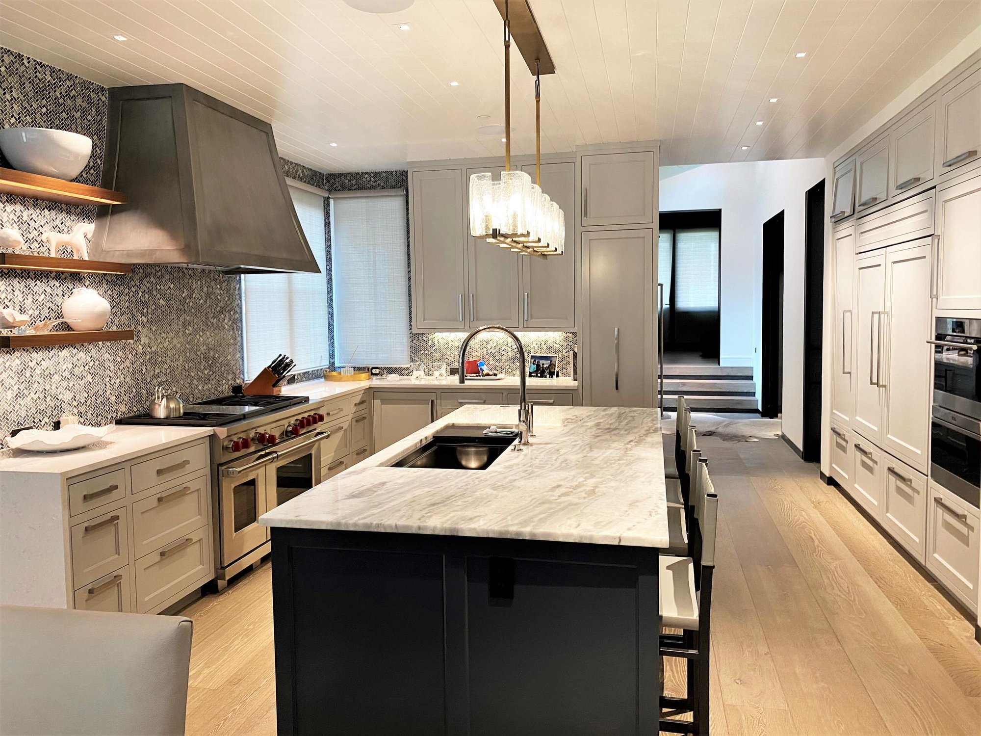 Large trendy u-shaped light wood floor, brown floor and shiplap ceiling open concept kitchen with an undermount sink, recessed-panel cabinets, white cabinets, gray backsplash, paneled appliances, an island and white countertops, by Jensen Design in Telluride, CO