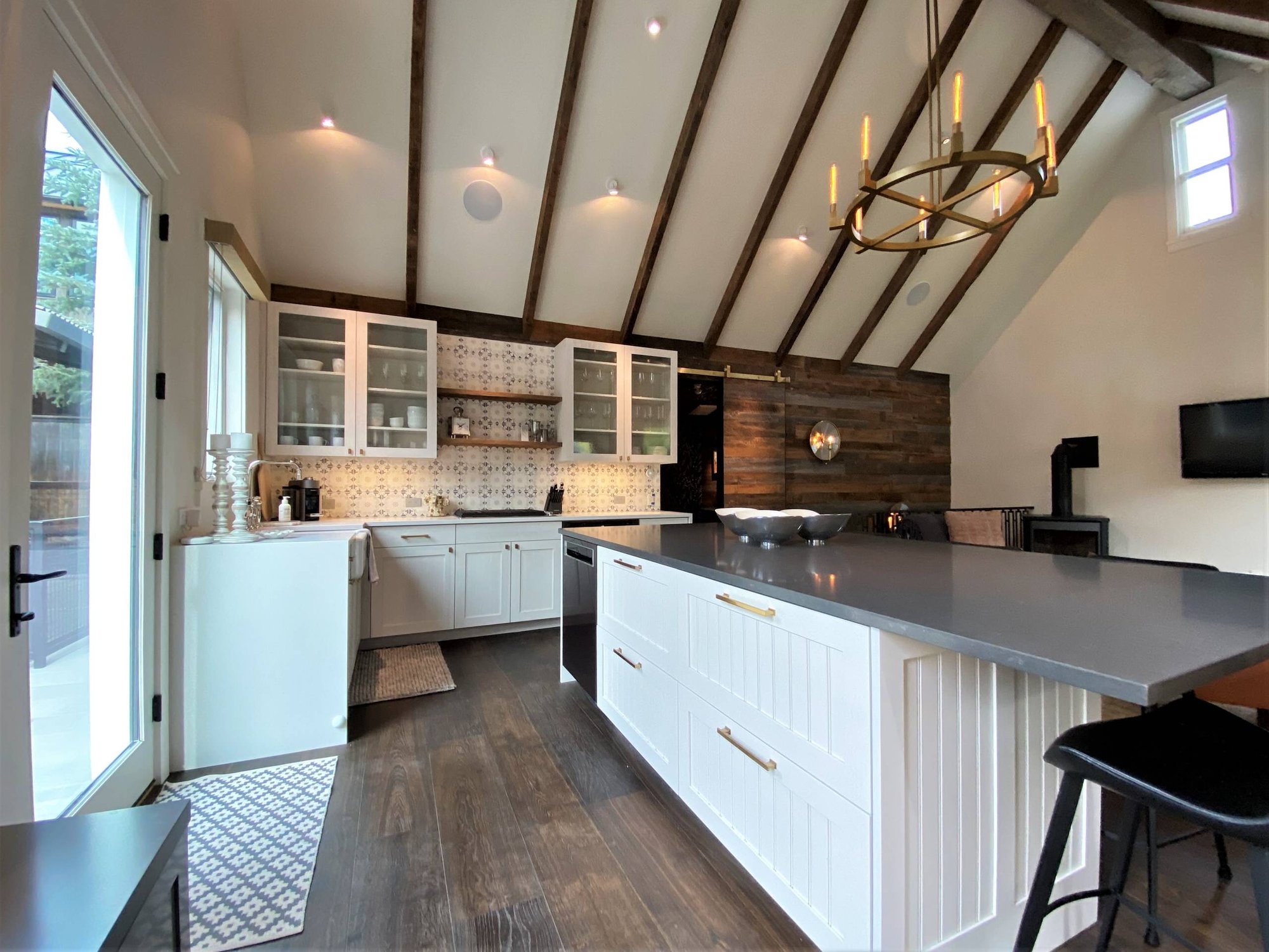 Mid-sized trendy l-shaped dark wood floor, brown floor and vaulted ceiling open concept kitchen with a farmhouse sink, recessed-panel cabinets, white cabinets, white backsplash, paneled appliances and an island, by Jensen Design in Telluride, CO