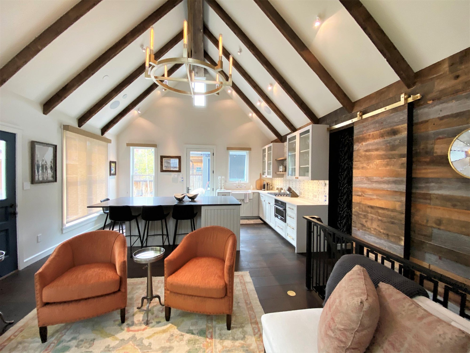 Mid-sized contemporary l-shaped dark wood floor, brown floor and vaulted ceiling open concept kitchen with a farmhouse sink, recessed-panel cabinets, white cabinets, white backsplash, paneled appliances and an island, by Jensen Design in Telluride, CO