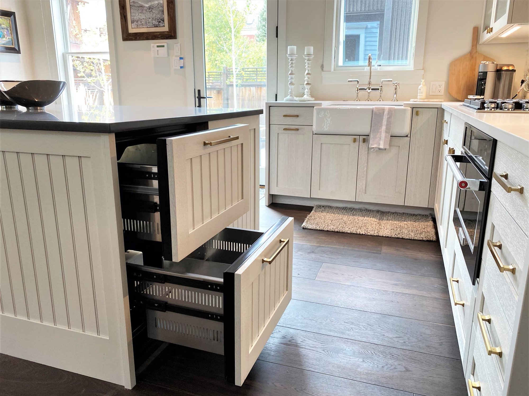 Mid-sized contemporary l-shaped dark wood floor, brown floor and vaulted ceiling open concept kitchen with a farmhouse sink, recessed-panel cabinets, white cabinets, white backsplash, paneled appliances and an island, by Jensen Design in Telluride, CO