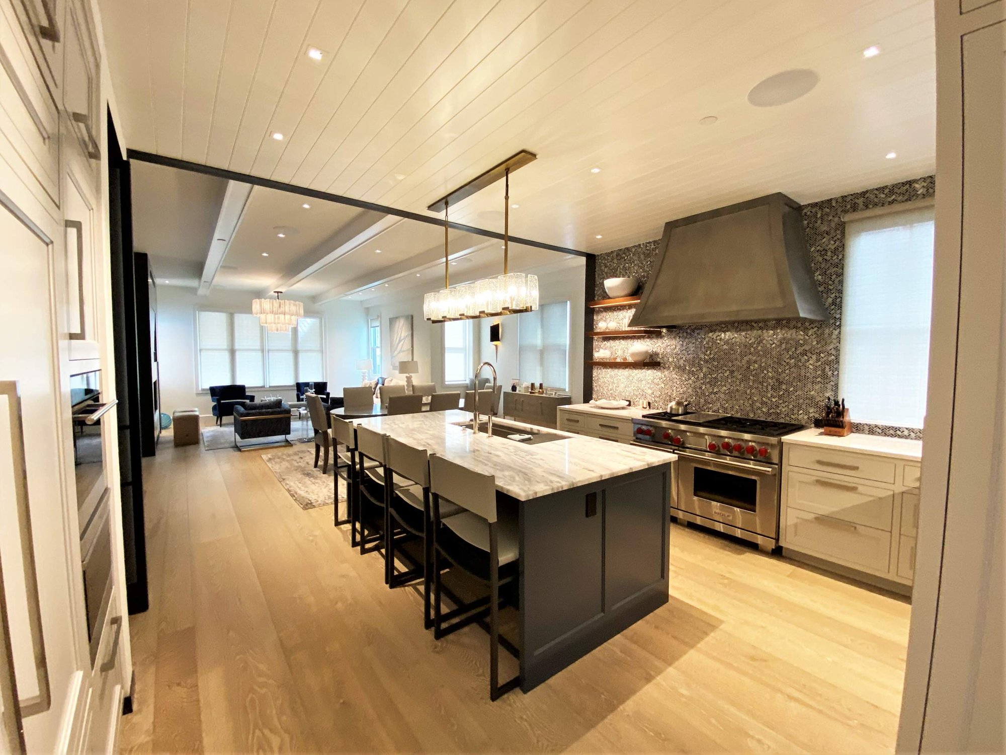 Large contemporary u-shaped light wood floor, brown floor and shiplap ceiling open concept kitchen with an undermount sink, recessed-panel cabinets, white cabinets, gray backsplash, paneled appliances, an island and white countertops, by Jensen Design in Telluride, CO