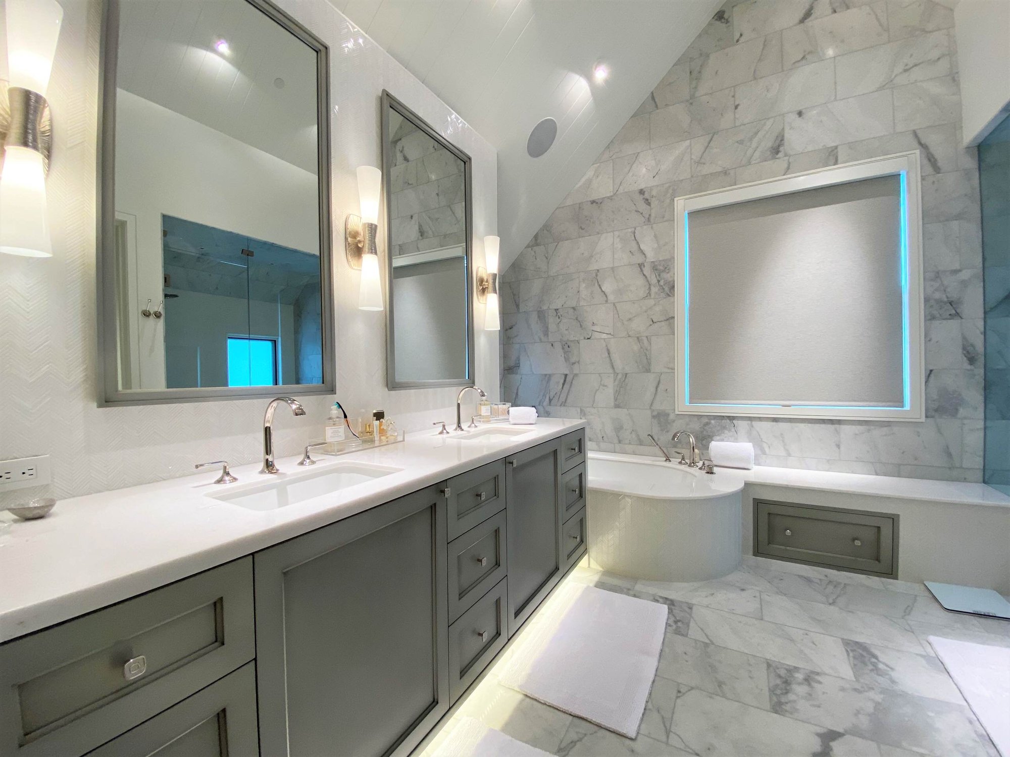 Large contemporary master white tile marble floor, white floor, double-sink and vaulted ceiling bathroom with recessed-panel cabinets, gray cabinets, an undermount tub, a one-piece toilet, white walls, an undermount sink, a hinged shower door, white countertops and a built-in vanity, by Jensen Desig