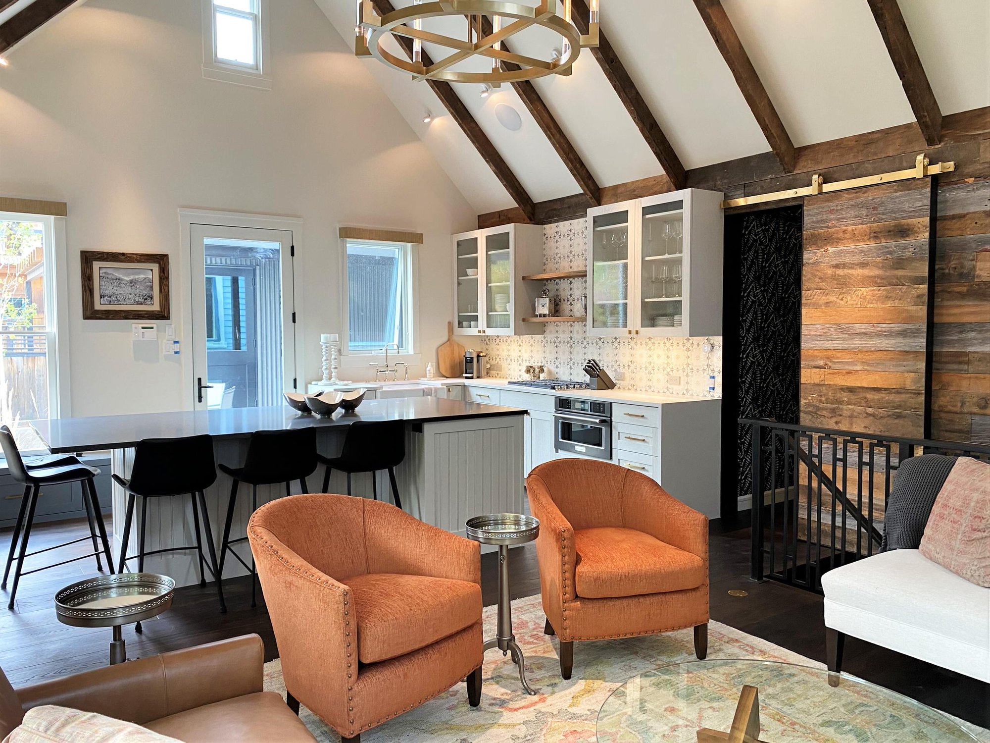 Mid-sized trendy l-shaped dark wood floor, brown floor and vaulted ceiling open concept kitchen with a farmhouse sink, recessed-panel cabinets, white cabinets, white backsplash, paneled appliances and an island, by Jensen Design in Telluride, CO