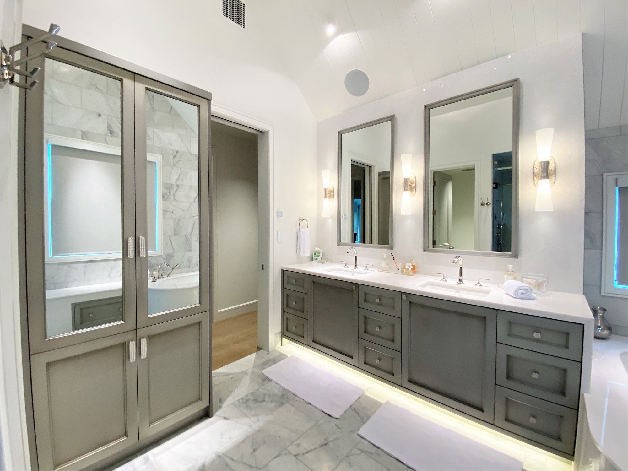 Large contemporary master white tile marble floor, white floor, double-sink and vaulted ceiling bathroom with recessed-panel cabinets, gray cabinets, an undermount tub, a one-piece toilet, white walls, an undermount sink, a hinged shower door, white countertops and a built-in vanity, by Jensen Desig