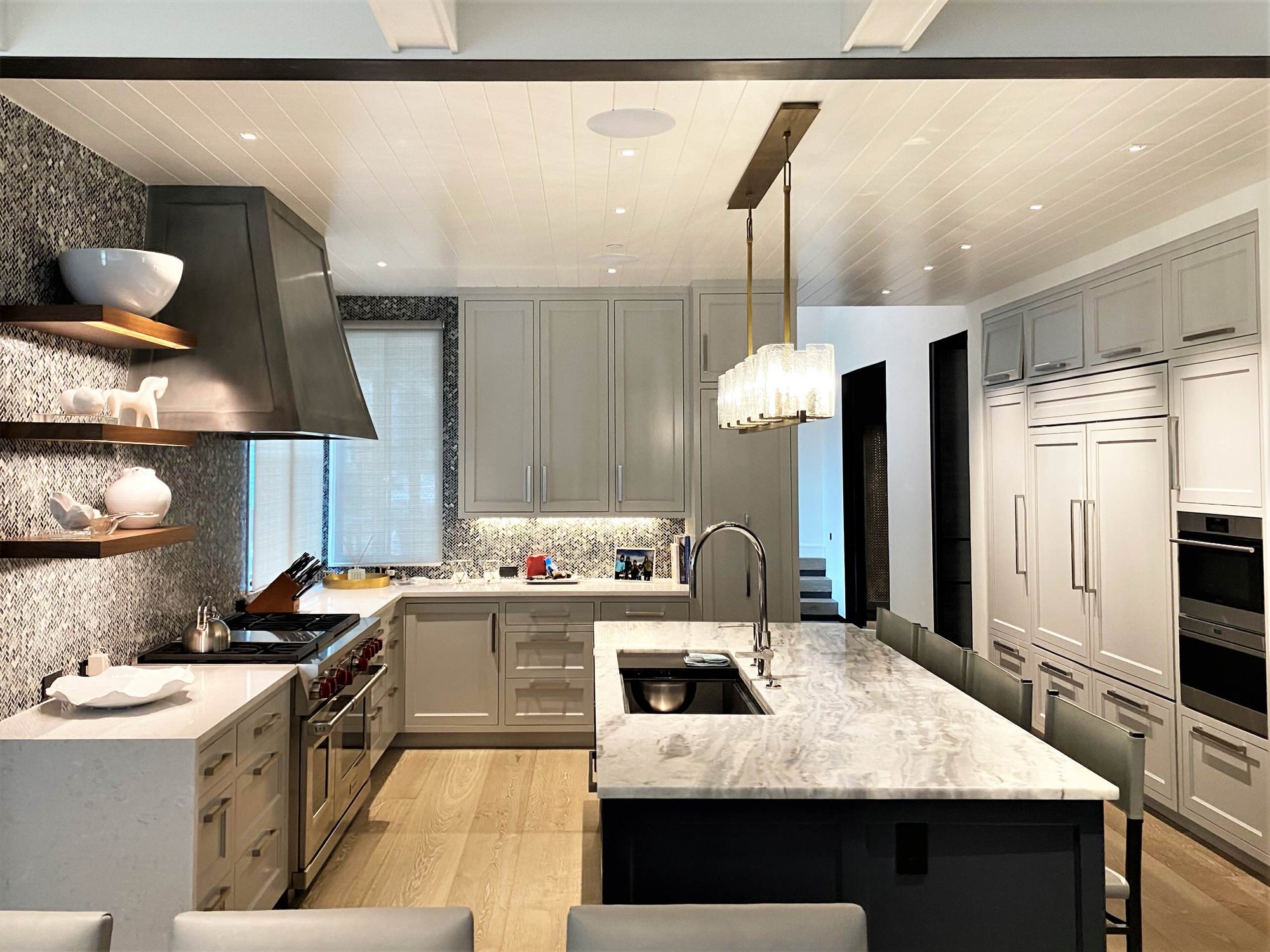 Large contemporary u-shaped light wood floor, brown floor and shiplap ceiling open concept kitchen with an undermount sink, recessed-panel cabinets, white cabinets, gray backsplash, paneled appliances, an island and white countertops, by Jensen Design in Telluride, CO
