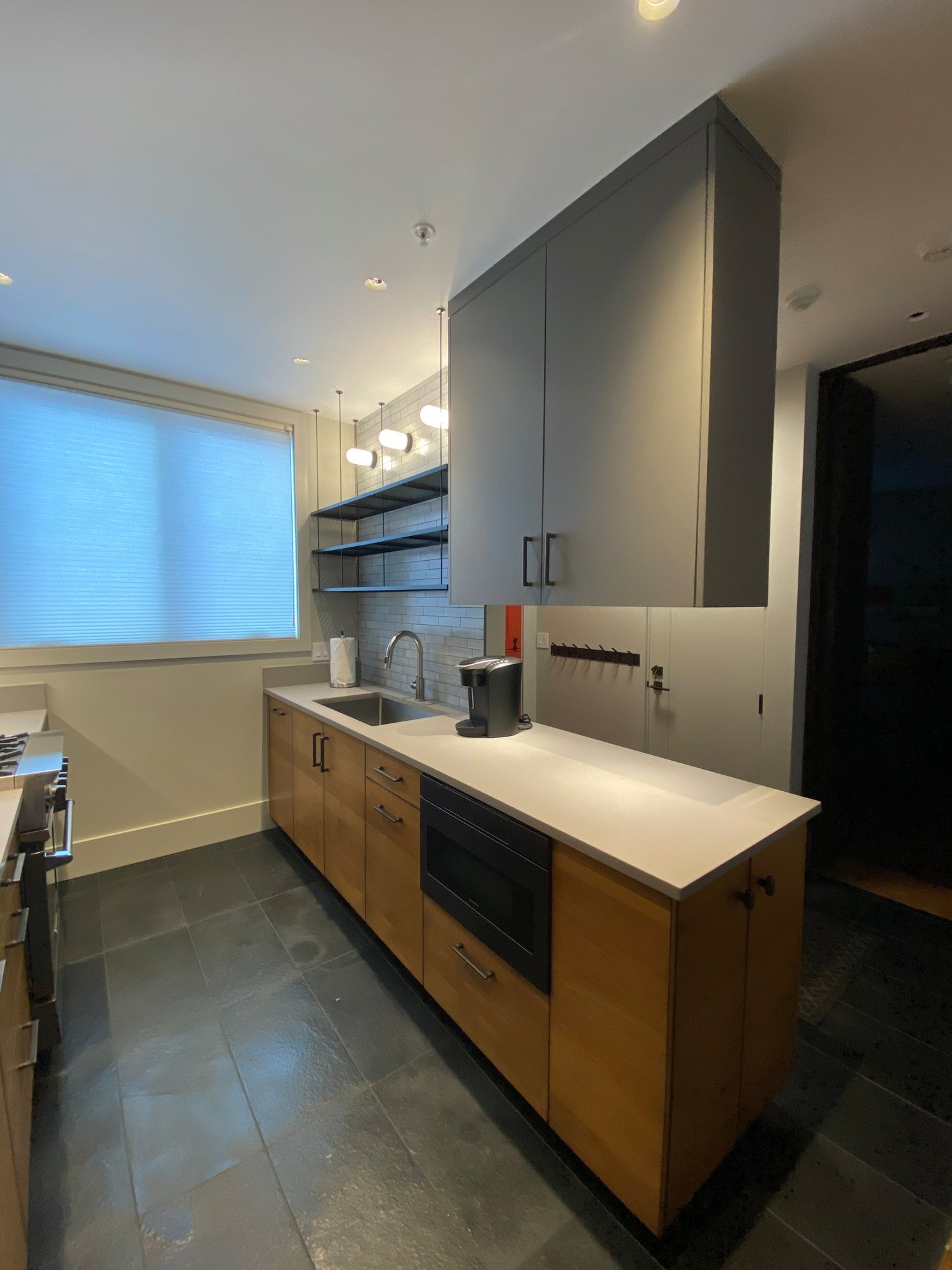 Small 1950s u-shaped black floor open concept kitchen with an undermount sink, flat-panel cabinets, medium tone wood cabinets, concrete countertops, white backsplash, stainless steel appliances and white countertops, by Jensen Design in Telluride, CO