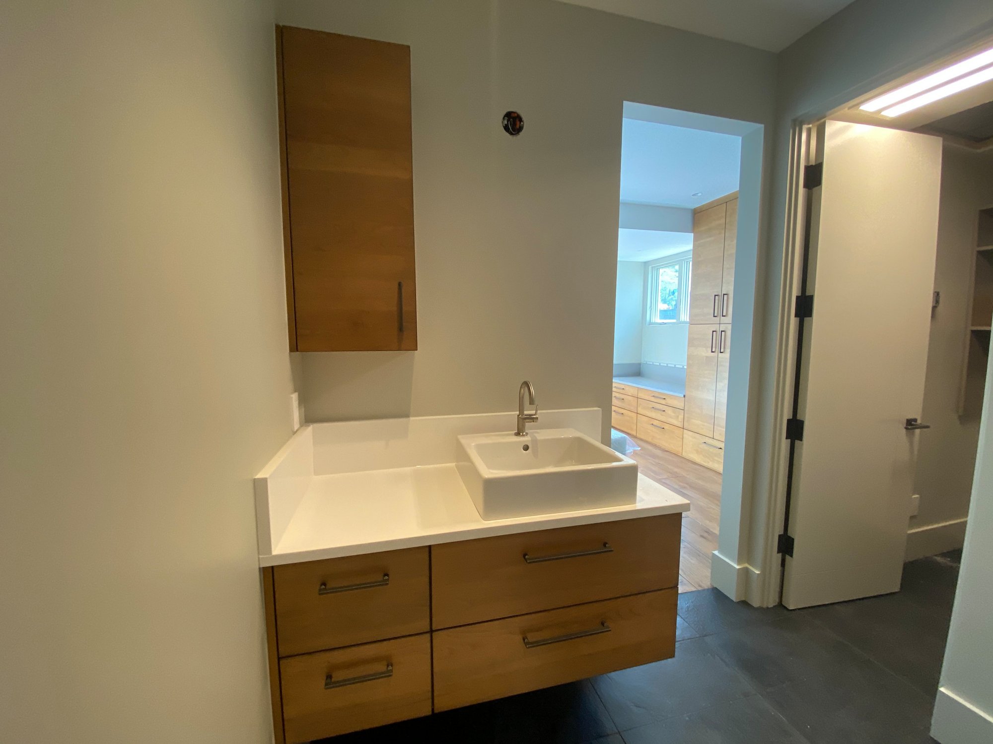 Small 1960s kids' black floor and single-sink bathroom with flat-panel cabinets, medium tone wood cabinets, beige walls, a vessel sink, white countertops and a floating vanity, by Jensen Design in Telluride, CO