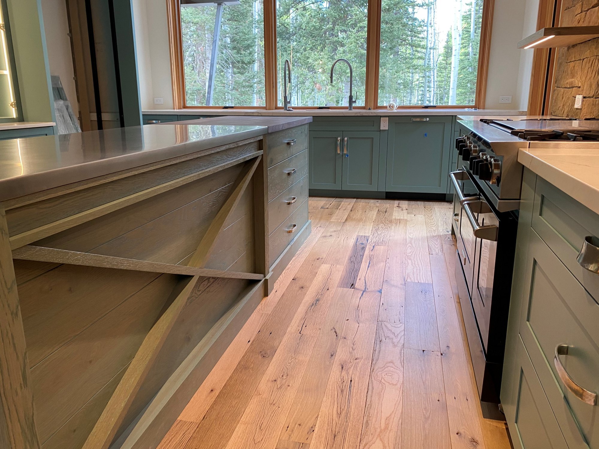 Mid-sized eclectic u-shaped medium tone wood floor, brown floor and exposed beam eat-in kitchen with an undermount sink, shaker cabinets, green cabinets, an island and white countertops, by Jensen Design in Telluride, CO
